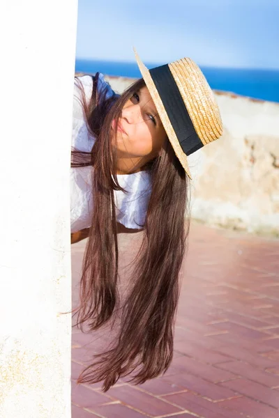 Girl in straw hat peeks out from behind wall — Stock Photo, Image