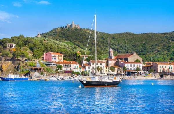 COLLIOURE, FRANÇA - JULHO 5, 2016: Hotéis de barco e praia na aldeia de Collioure com um moinho de vento no topo da colina, Roussillon, Vermilion coast, Pyrenees Orientales, França — Fotografia de Stock