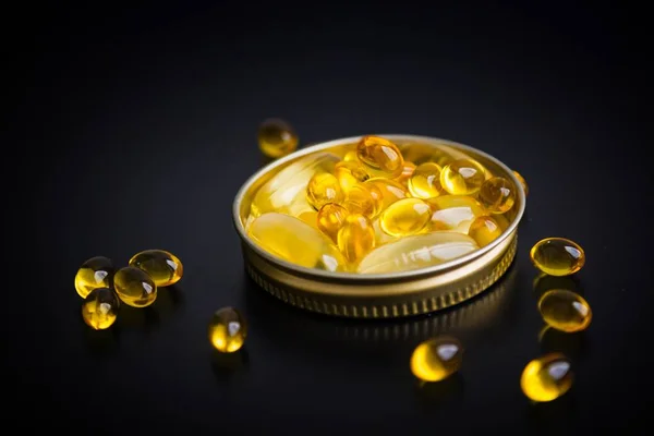 Capsules of fish oil in gold cup on black background