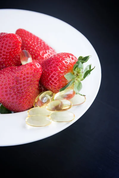 Fresh strawberries and capsules of fish oil on black — Stock Photo, Image