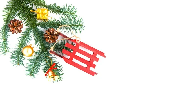 Decoraciones navideñas y rama de árbol sobre fondo blanco. Trineo rojo, conos, regalo de oro, campana y pelota. Copiar espacio. Acostado. Año Nuevo y estado de ánimo de Navidad —  Fotos de Stock