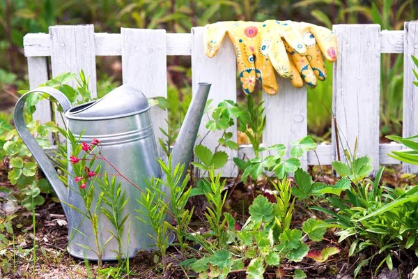 Venkovní zahradnické nářadí na zahradě na jaře. Zavlažovací plechovka, barevné rukavice na zemi — Stock fotografie