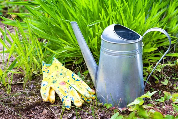 Outdoor gardening tools in garden in spring. Watering can, colorful gloves on the ground