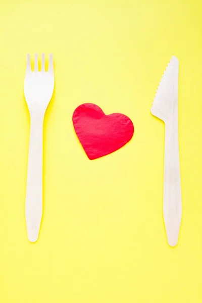 Bamboo biodegradable fork and knife made of natural eco recycle reusable material and paper heart on yellow. — Stock Photo, Image