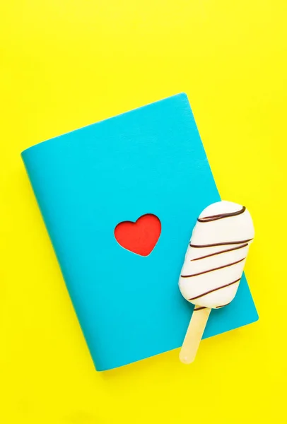 Blue notebook with red heart and popsicle on yellow. Saint Valentine`s day. — Stock Photo, Image