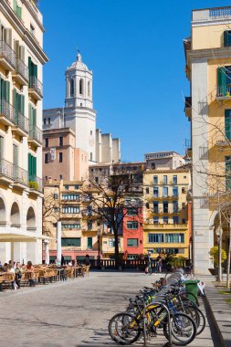 Girona, İspanya - 24 Şubat 2020: Girona Saint Mary Katedrali ve Independence Meydanı 'ndan renkli evler. Güneşli bir günde bisiklet parkı ve açık hava kafesi