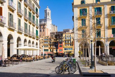 Girona, İspanya - 24 Şubat 2020: Girona Saint Mary Katedrali ve Independence Meydanı 'ndan renkli evler. Güneşli bir günde bisiklet parkı ve açık hava kafesi
