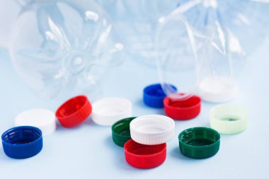 Şişelere karşı renkli plastik kapaklar. Mavi arka planda plastik ambalaj çöpü. Plastik ile çevre kirliliği kavramı.