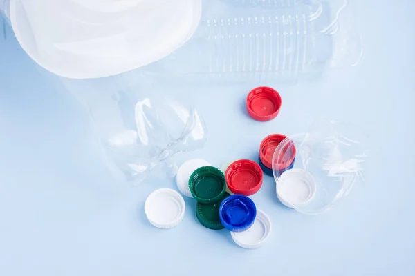 Colorful plastic caps against bottles. Plastic wrapping rubbish on blue background. Concept of environmental pollution with plastic.