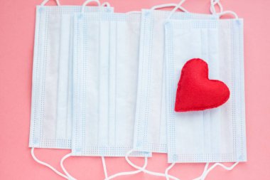 Pembe arka planda kırmızı kalpli mavi kumaş maskeler. Cesur yürek ve tüm tıp işçilerine minnettarlık. Coronavirus, COVID-19, karantina sırasında salgın. Hemşire günü
