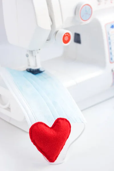 Red heart on mask face fabric. Health care and coronavirus protect with sew mask. Sewing medical masks to protect against coronavirus.Production of masks on sewing machine during quarantine