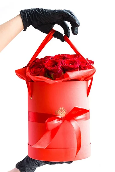 手戴黑色医用手套 纸盒里有红玫瑰 在大肠病毒大流行期间 在隔离过程中没有接触地送花 图库图片