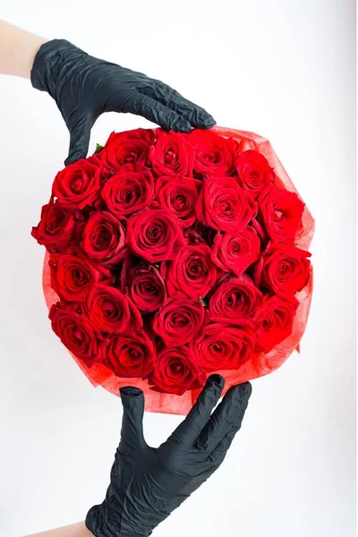 Hands in black medical gloves with red roses in paper box. Contactless flower delivery during isolation during coronavirus pandemic.