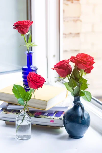 Stack of books and roses in vases near an open window. Quarantine. Social distance. Insulation