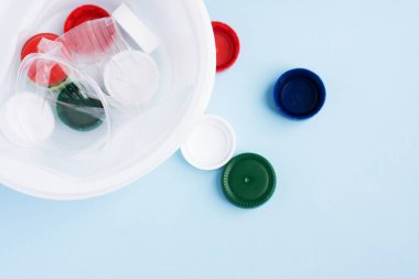 Renkli plastik kapaklar, tabaklar ve bardaklar şişelere karşı. Maviye plastik ambalaj çöpü. Plastikle çevre kirliliği kavramı. Bardağa odaklan.