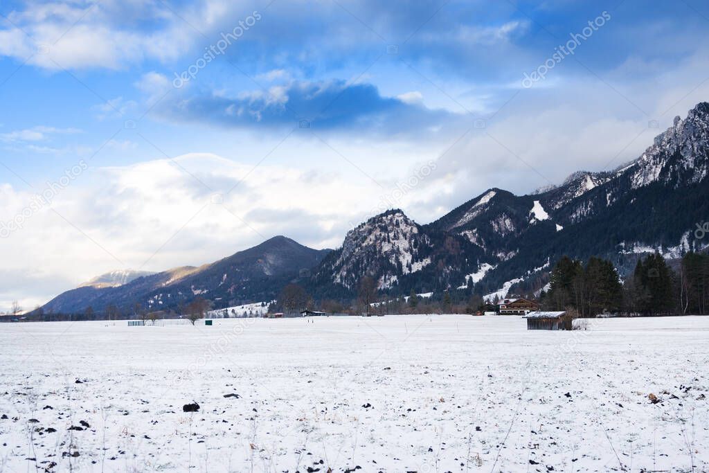 Wooden shed in snowy field against Alps in winter day. Schwangau, Bavaria, Germany