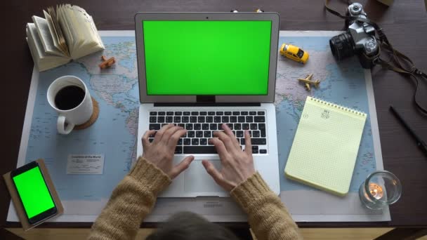 平面図です。世界地図をテーブル、女性の休暇を計画します。ノート パソコンと緑色の画面を持つスマート フォン — ストック動画