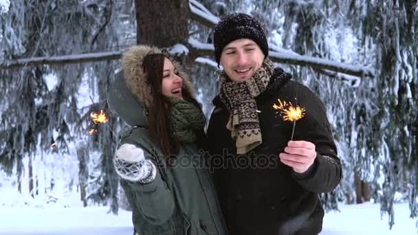 Winterpark. junges Liebespaar küsst sich, hält Wunderkerzen in der Hand und posiert für die Kamera — Stockvideo