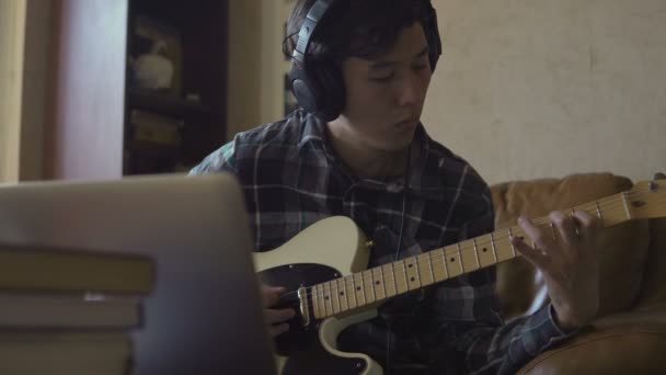 Um jovem toca guitarra, gravando música em casa — Vídeo de Stock