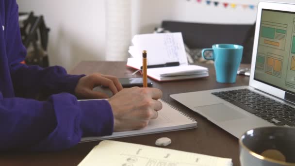 Freelancers workplace. Web Developer makes sketches of the site in his notebook working remotely from home office — Stock Video
