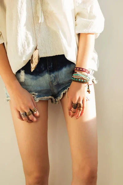 close up of women`s legs in boho style in denim shorts and a white blouse