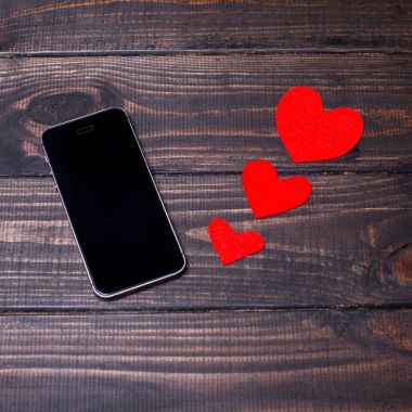 Siyah akıllı telefon ile boş perde ahşap arka plan üzerinde kırmızı mavi kalpler olan yalan. Sevgililer günü için kavram