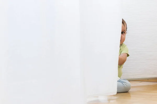 Barnet leker med vita gardiner — Stockfoto
