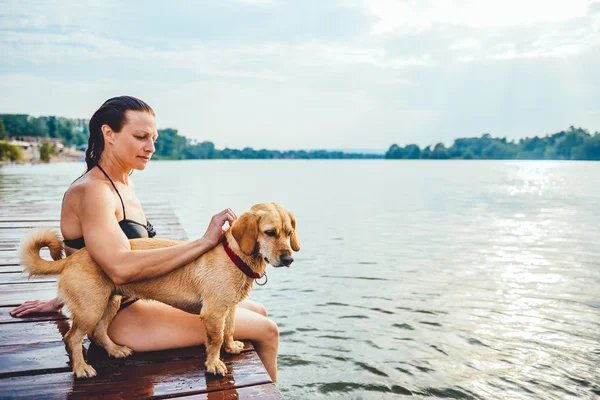 Kvinde sidder med hund på dock - Stock-foto