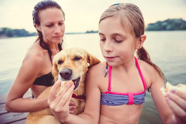 Niña Compartiendo Sándwich Con Perro Sentada Con Madre Junto Río — Foto de Stock