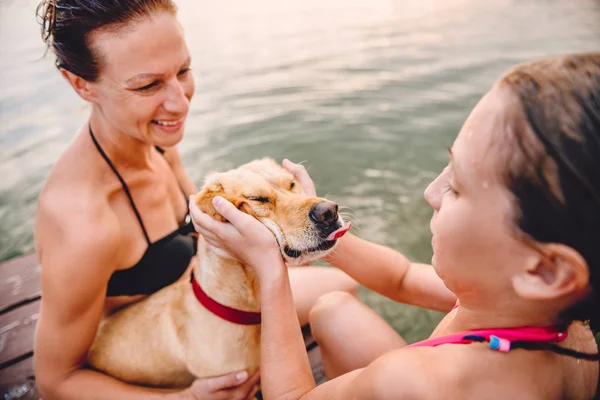 Hija Sentada Muelle Con Madre Abrazando Pequeño Perro Amarillo — Foto de Stock