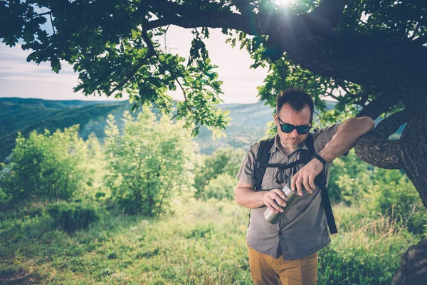 Muž Sobě Sluneční Brýle Batoh Odpočívá Pod Stromem Drží Láhev — Stock fotografie