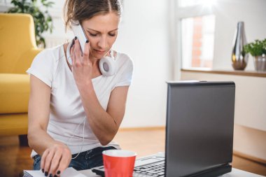 Masada oturan ve evde akıllı telefonda konuşurken beyaz gömlek giyen kadın