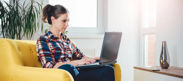 여자는 거실에서 노란색 소파에 앉아서 노트북을 — 스톡 사진