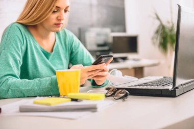 Ofiste masada oturan ve akıllı telefon kullanan kadın