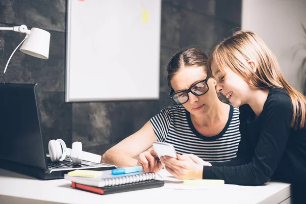 Mother and daughter using smart phone at home office