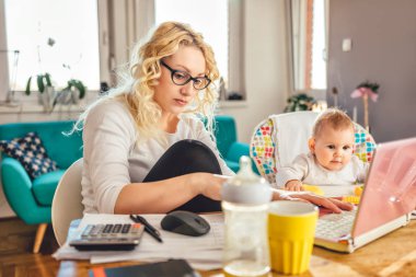 Evde ofis dizüstü bilgisayarda çalışan ve onun Bebek Bakımı gözlük takmış anne