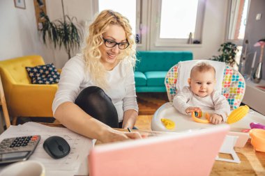 Evde ofis dizüstü bilgisayarda çalışan ve onun Bebek Bakımı gözlük takmış anne