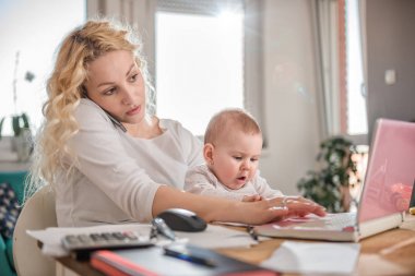 Anne bebek tutan, office evde akıllı telefonda konuşurken ve dizüstü bilgisayar kullanarak