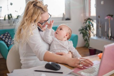 Anne bebek tutan, office evde akıllı telefonda konuşurken ve dizüstü bilgisayar kullanarak