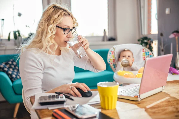 Madre Vistiendo Anteojos Sentada Escritorio Con Bebé Bebiendo Agua Mientras — Foto de Stock