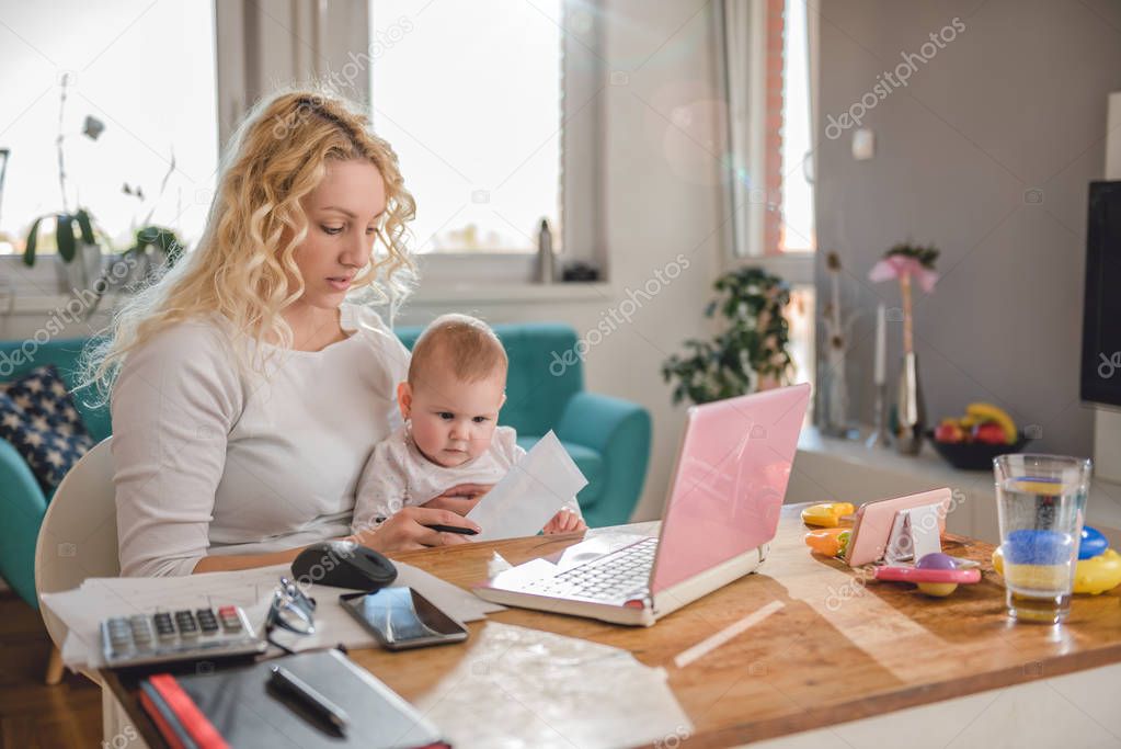 Mother working at home office and taking care of her baby
