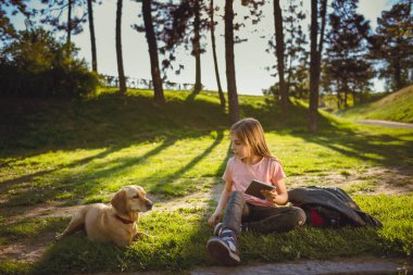 Kız ile bir köpek parkta oturan ve tablet kullanma