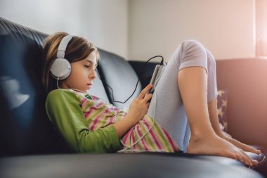 Tablet kullanma ve müzik dinleme siyah koltukta oturan kız