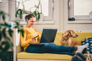 Evde sarı koltukta oturan ve kredi kartı ile alışveriş online sarı kazak giyen kadın. 