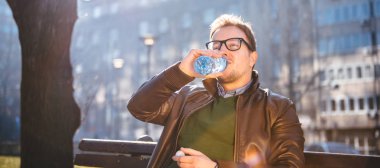 Adam bankta oturan ve plastik Şişeden içme suyu