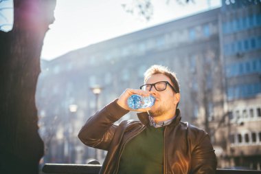 Adam bankta oturan ve plastik Şişeden içme suyu