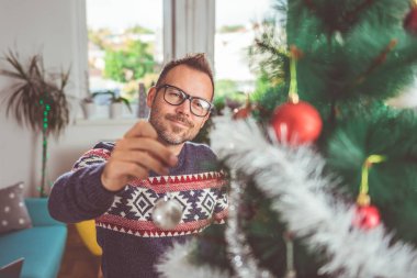 yakışıklı adam Mavi kazak ve Noel ağacı evde dekorasyon gözlük takıyor