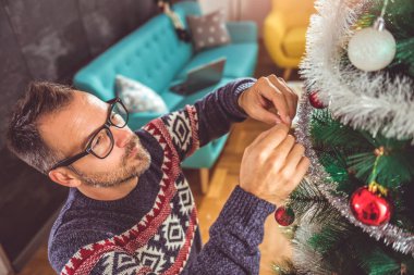 yakışıklı adam Mavi kazak ve Noel ağacı evde dekorasyon gözlük takıyor