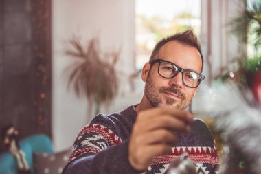 yakışıklı adam Mavi kazak ve Noel ağacı evde dekorasyon gözlük takıyor