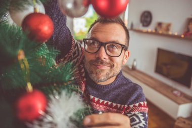 yakışıklı adam Mavi kazak ve Noel ağacı evde dekorasyon gözlük takıyor